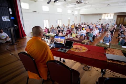 A monk guiding meditation for a large audience in a community hall